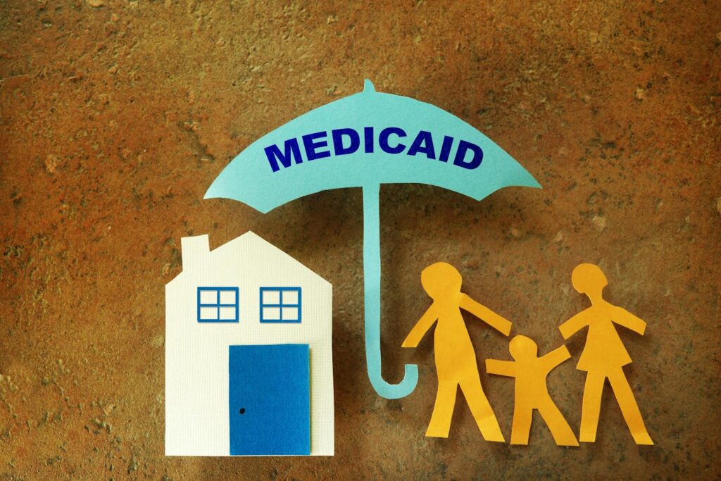 Paper cutout of a Medicaid umbrella sheltering a house and family
