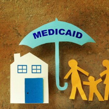 Paper cutout of a Medicaid umbrella sheltering a house and family